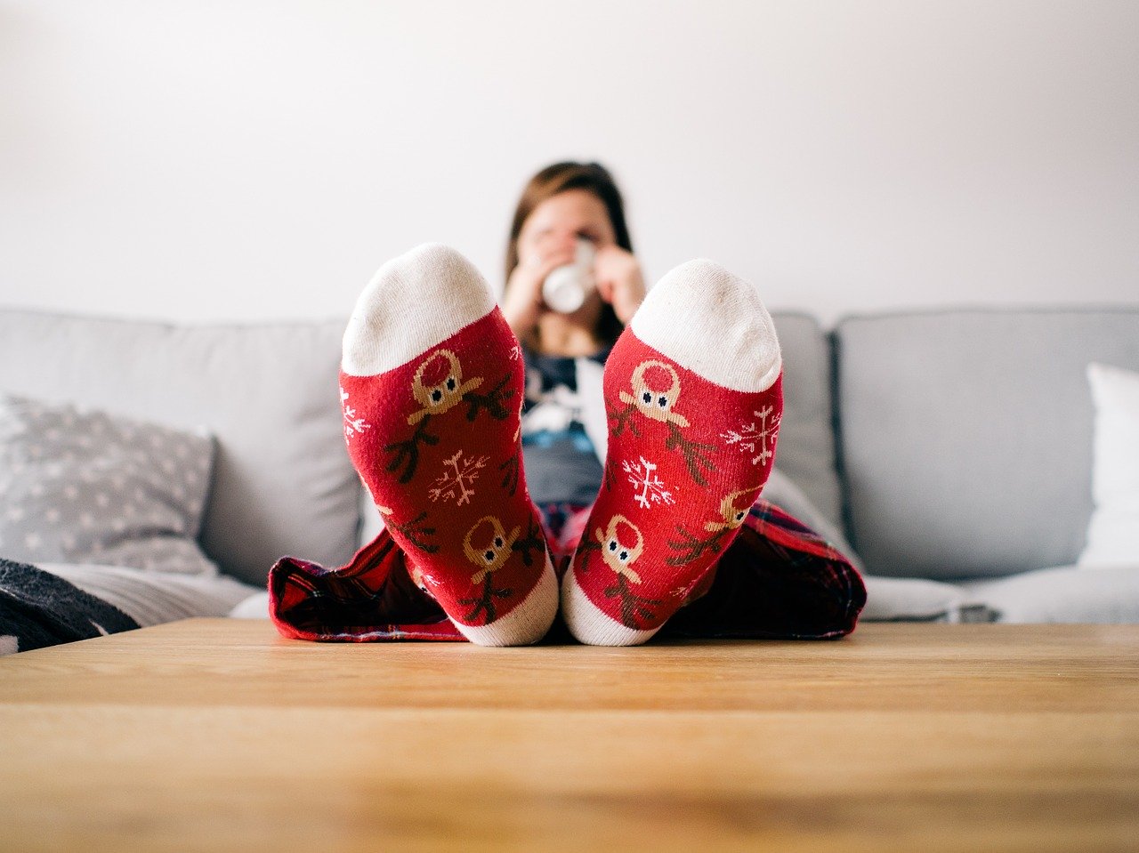 Uma mulher tomando café sentada no sofá com os pés escorados na mesa. Imagem de tookapic por Pixabay