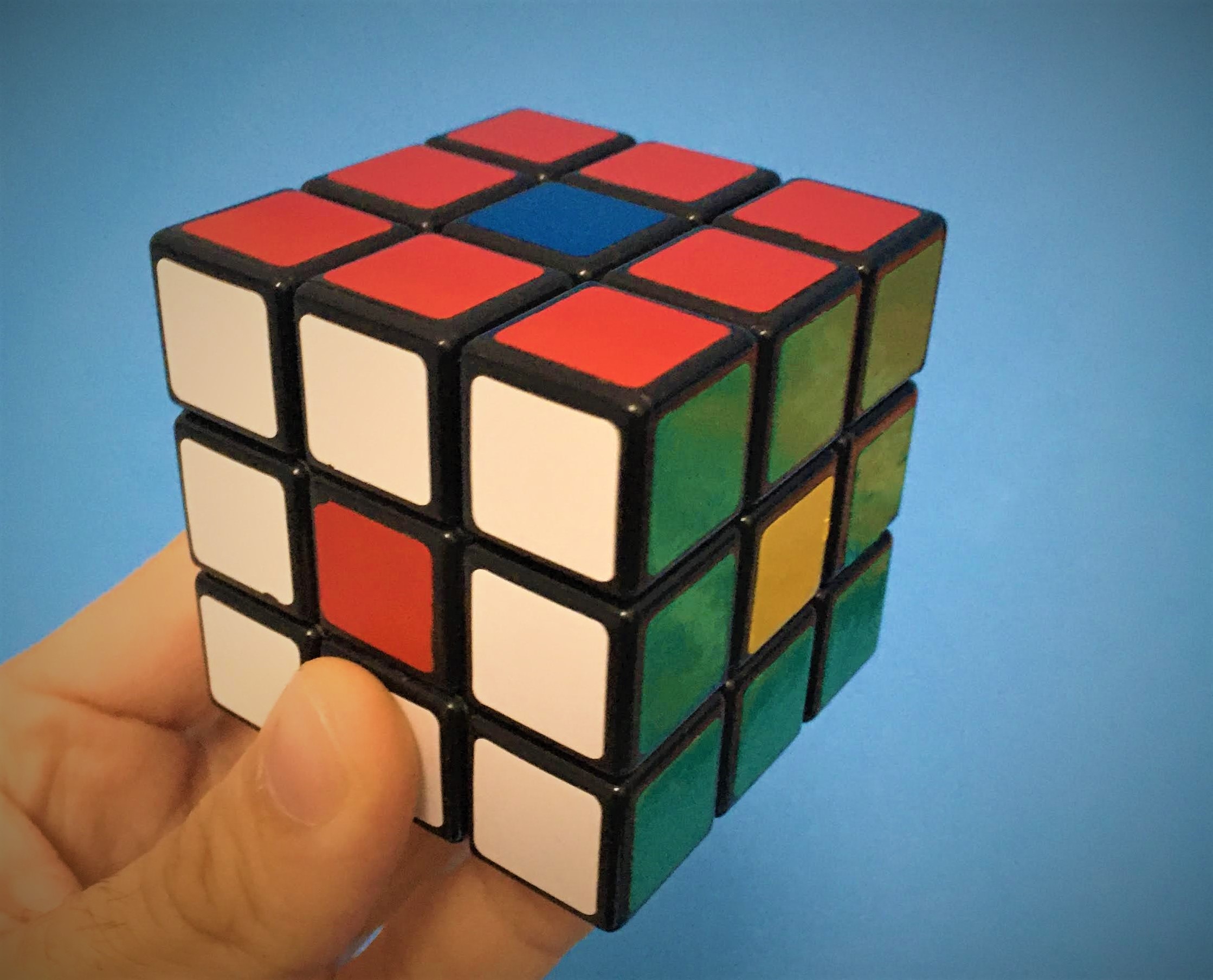 Uma mão segurando o cubo de Rubik com as cores posicionadas de maneira invertida em relação à cor do centro.