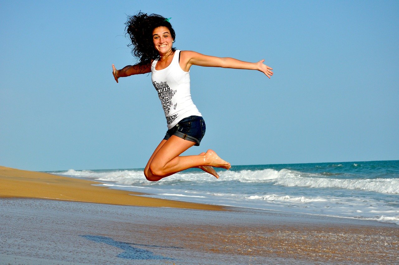 Uma mulher dando um salto numa praia e a câmera capturou o exato momento que ela está no ar.