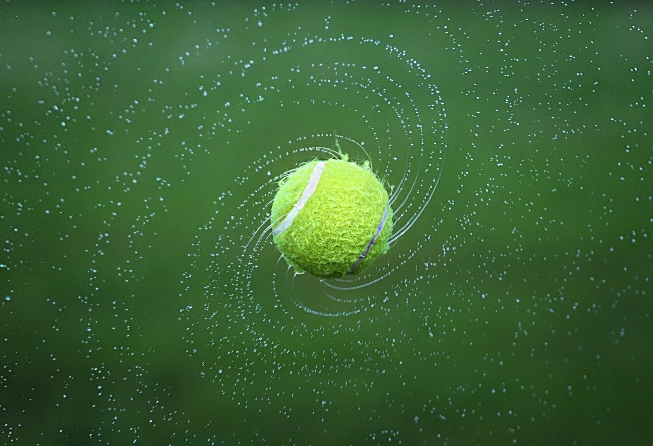 Autismo Frases. Descrição da imagem. Uma bola de tênis verde molhada girando no ar e espalhando gotículas de água em forma de espiral.